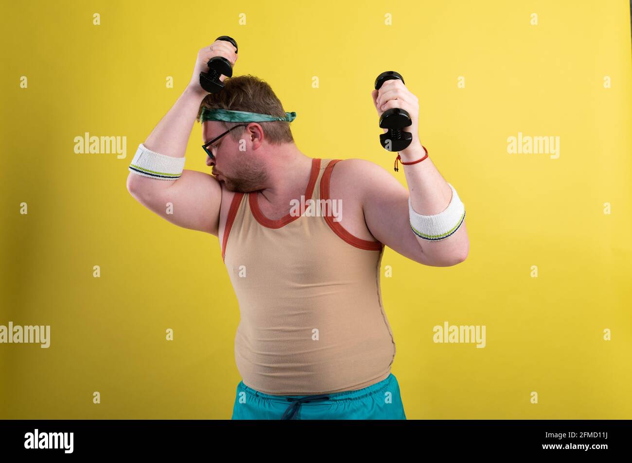 divertente uomo grasso va in per lo sport. Fa un esercizio di bicipiti di manubri Foto Stock