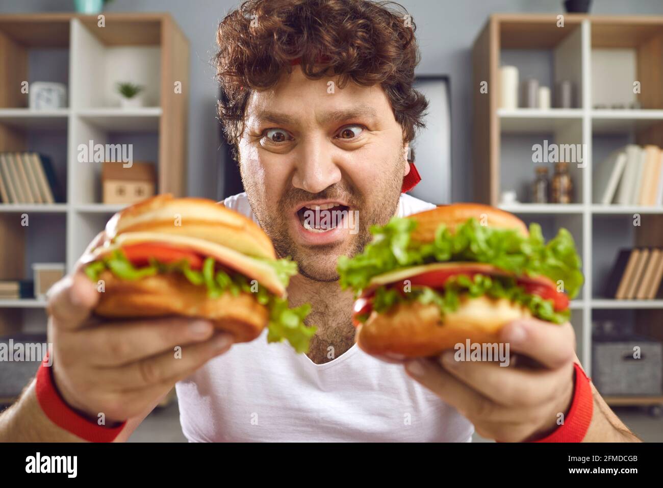 Affamato uomo chubby guardando due deliziosi hamburger con divertente espressione della faccia Foto Stock