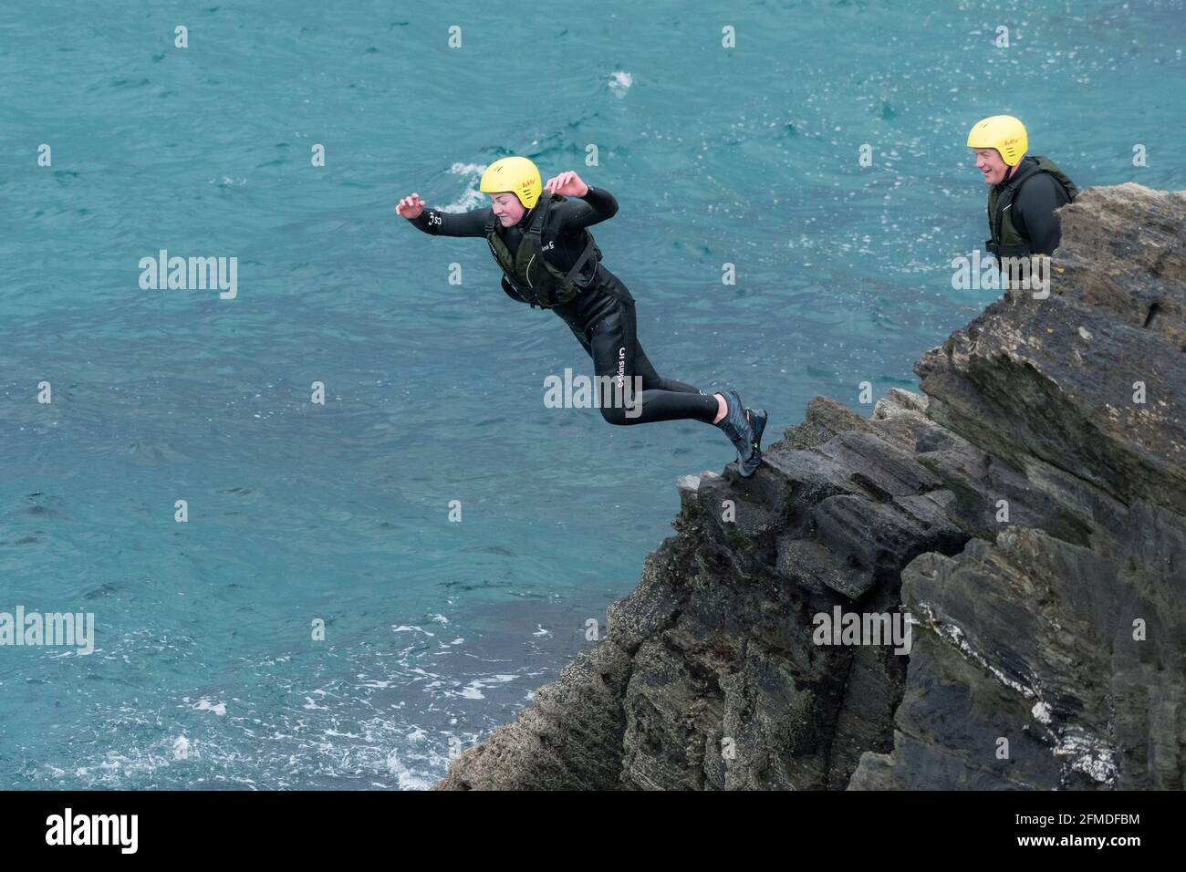 Un giovane turista che salta in mare dalle rocce in un viaggio di coastering intorno a Towan Head a Newquay in Cornovaglia. Foto Stock