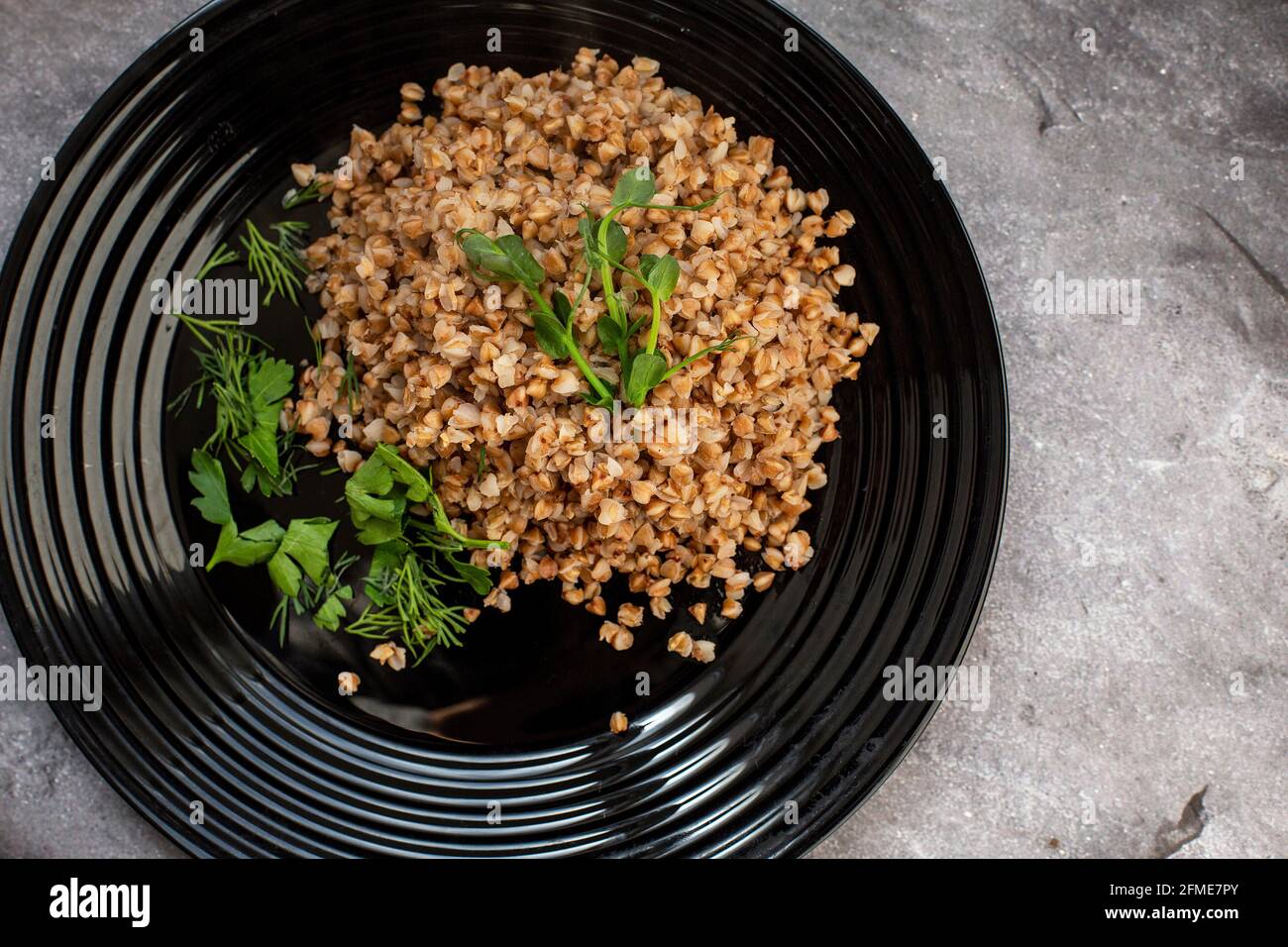 porridge di grano saraceno bollito con erbe e germogli di piselli su un piatto nero. Foto Stock