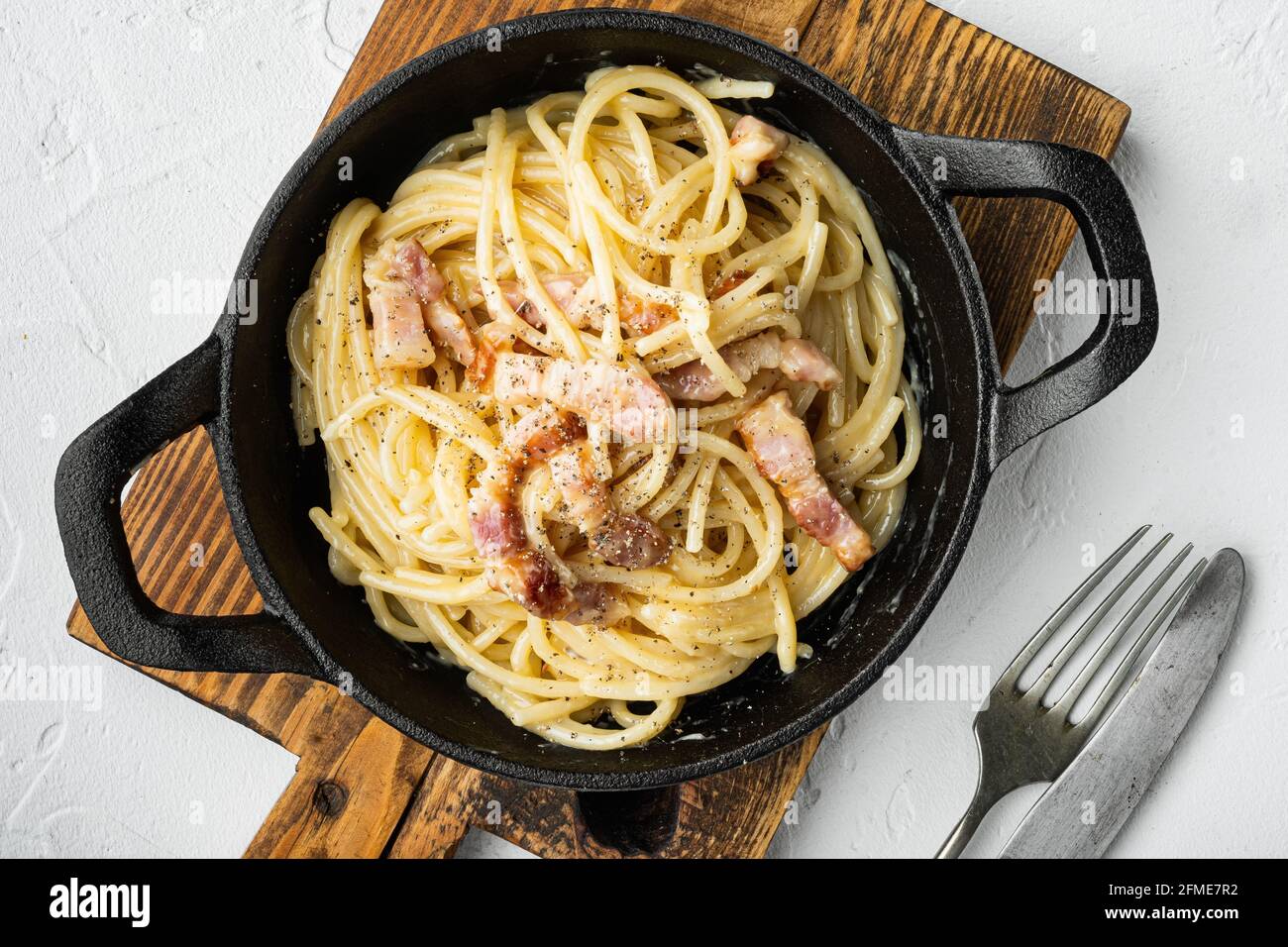 Carbonara pasta. Spaghetti con frittella, uovo, parmigiano, in padella di  ghisa, su superficie di pietra bianca Foto stock - Alamy