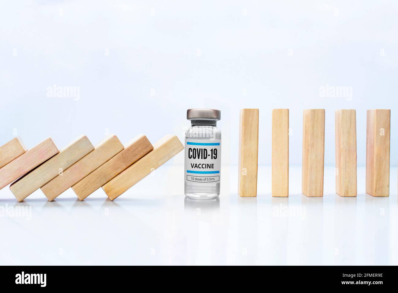 Pezzi di legno effetto domino arresto caduta con un vaccino Covid-19 flaconcino, accanto allo stand pezzi di legno concetto: Vaccino Covid-19 fermare crisi e rischio Foto Stock