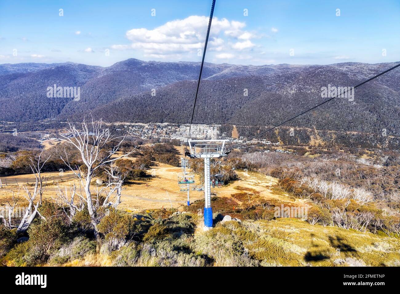 Seggiovia che scende al villaggio di Thredbo da alture di montagne innevate in Australia - soleggiato giorno d'autunno. Foto Stock