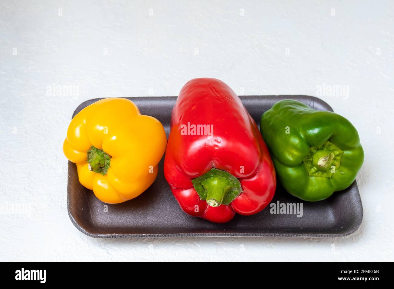 Tre peperoni dolci bulgari rossi gialli e verdi in un contenitore su sfondo chiaro, primo piano. Il concetto di cibo sano, dieta, peso co Foto Stock