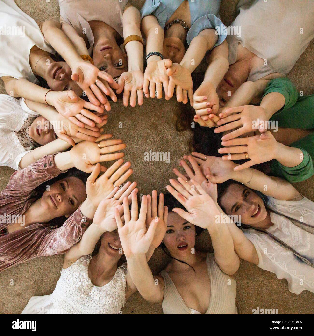 Felici amici donne che giacciono a cerchio alzando le mani insieme godendo di amicizia collaborazione Foto Stock