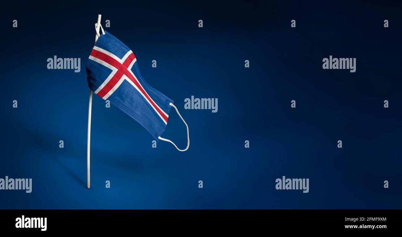 Maschera islandese su sfondo blu scuro. Bandiera ondulata dell'Islanda dipinta su maschera medica sul palo. Flag di attacco del virus. Concetto del banner della Fight ag Foto Stock