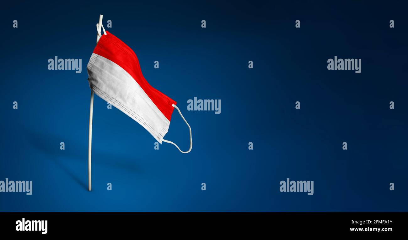 Maschera Indonesia su sfondo blu scuro. Bandiera ondulata dell'Indonesia dipinta su maschera medica sul palo. Flag di attacco del virus. Concetto della bandiera della coscia Foto Stock