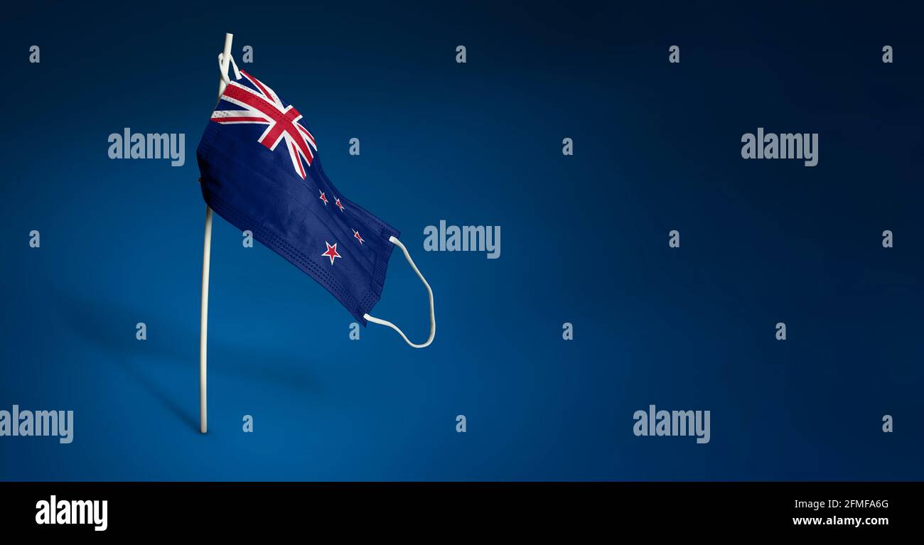Maschera neozelandese su sfondo blu scuro. Bandiera ondulata della Nuova Zelanda dipinta su maschera medica sul palo. Flag di attacco del virus. Concetto del banner del Foto Stock