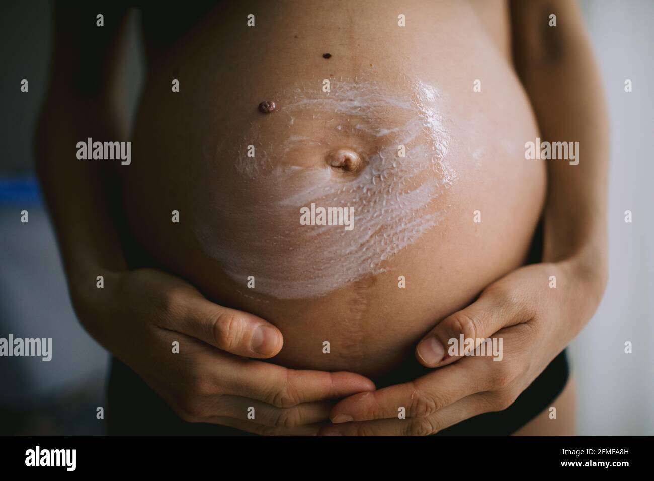 Donne incinte che mettono la crema anti stirata sul suo ventre. Cosmetici per idratare o idratare la pelle in gravidanza. Foto Stock