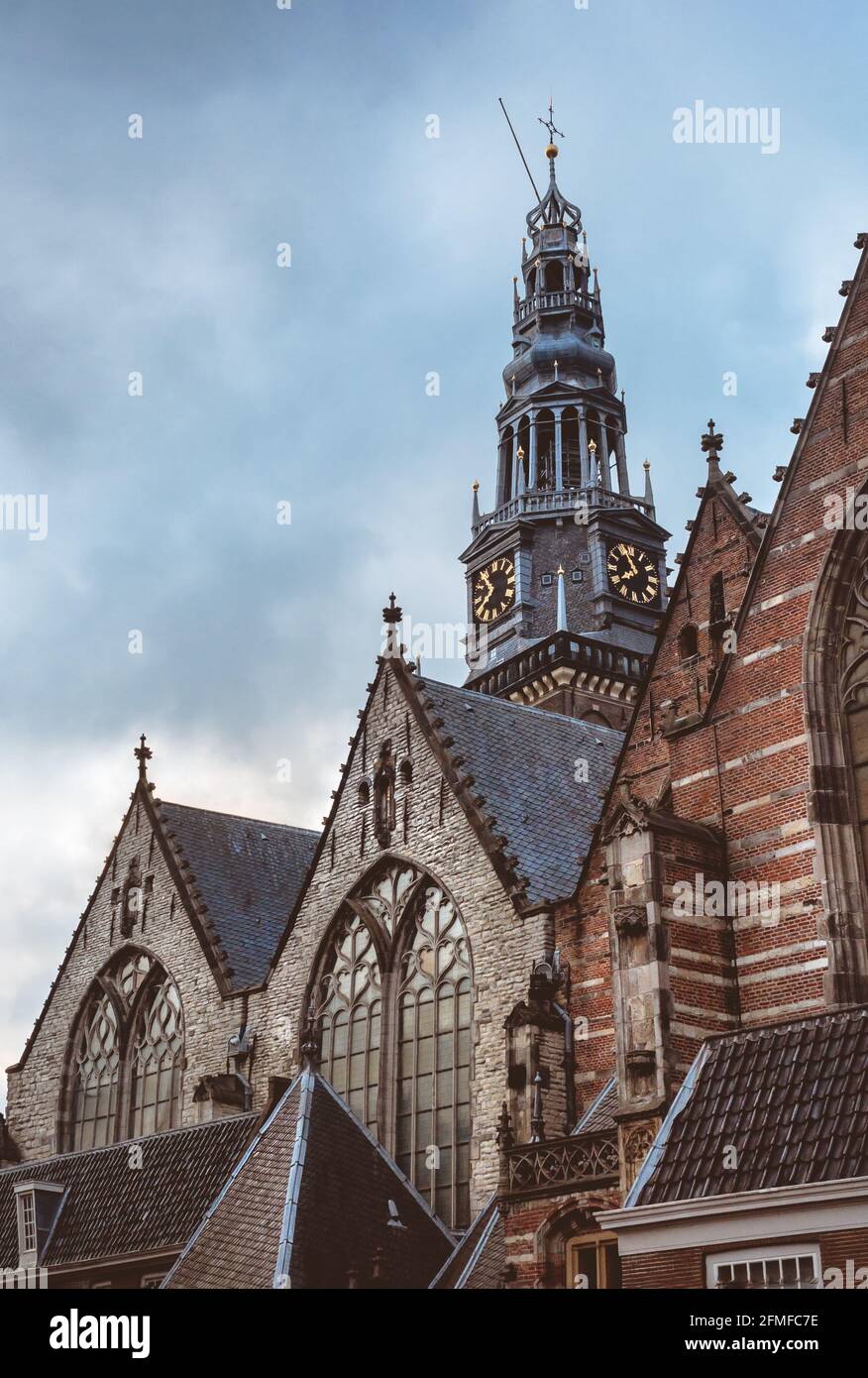 Finestre gotiche e tetti in tegole della chiesa Calvinista Oude Kerk e vecchio campanile con orologio al cielo nuvoloso. Architettura cristiana antica e churc Foto Stock