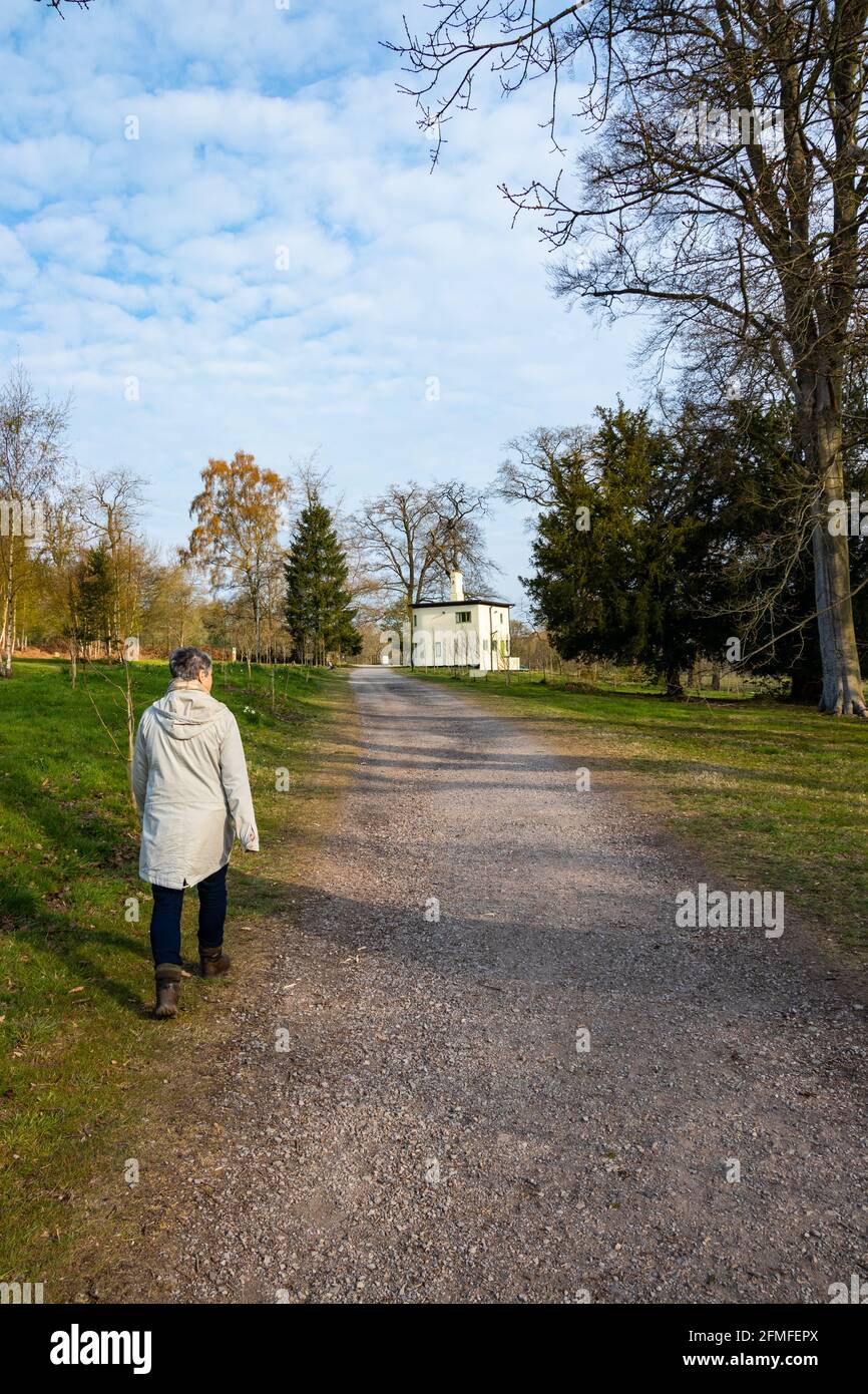 donna di mezza età che cammina lungo il percorso in alberi verso isolato Casa a Trentham Gardens vicino a Stoke su Trent Staffordshire Foto Stock