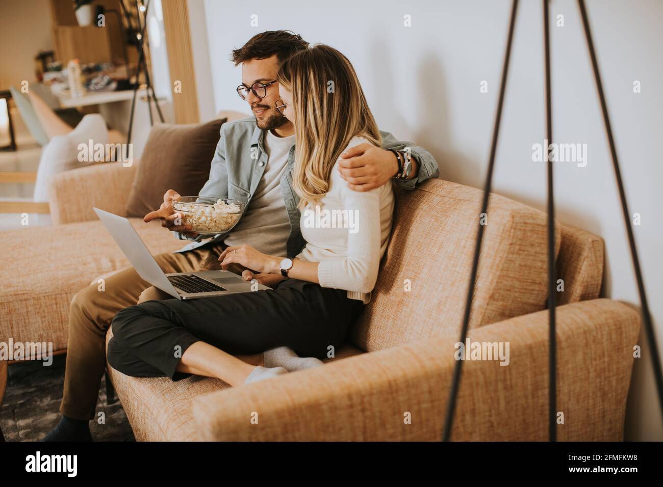Bella giovane coppia che usa il computer portatile insieme mentre si siede sul divano a casa Foto Stock