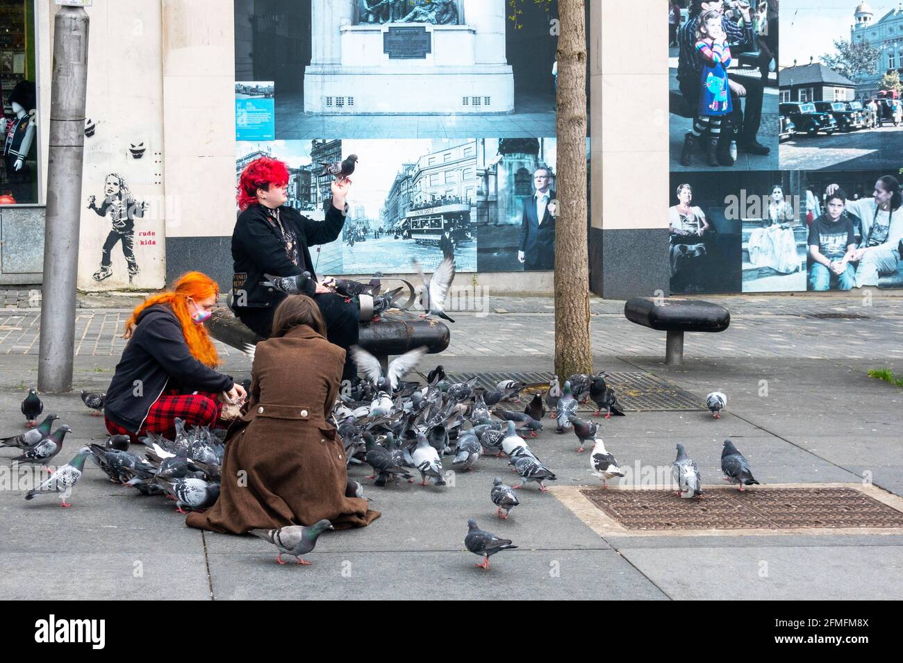 Tre giovani donne che nutrono i piccioni in una strada a Liverpool Foto Stock
