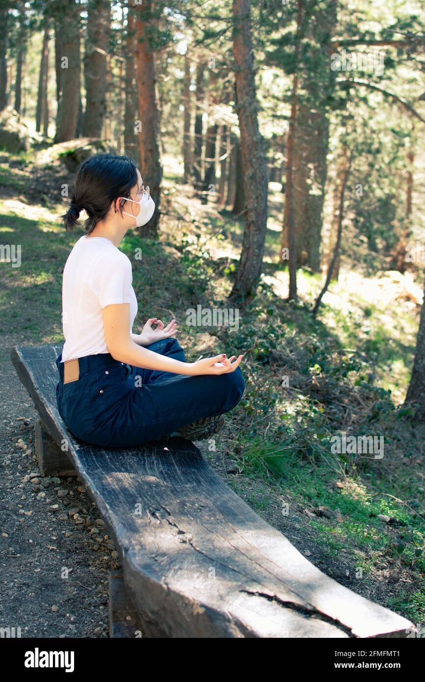 Vista laterale di una donna che fa yoga nella foresta mentre indossa una maschera. Foto verticale. Foto Stock