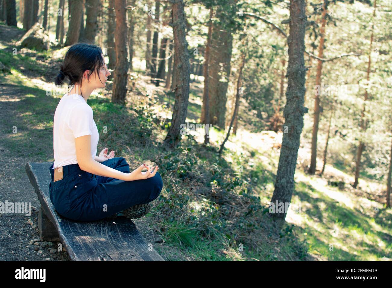 Vista laterale di una giovane donna seduta su una panchina mentre fa yoga nella foresta. Foto Stock