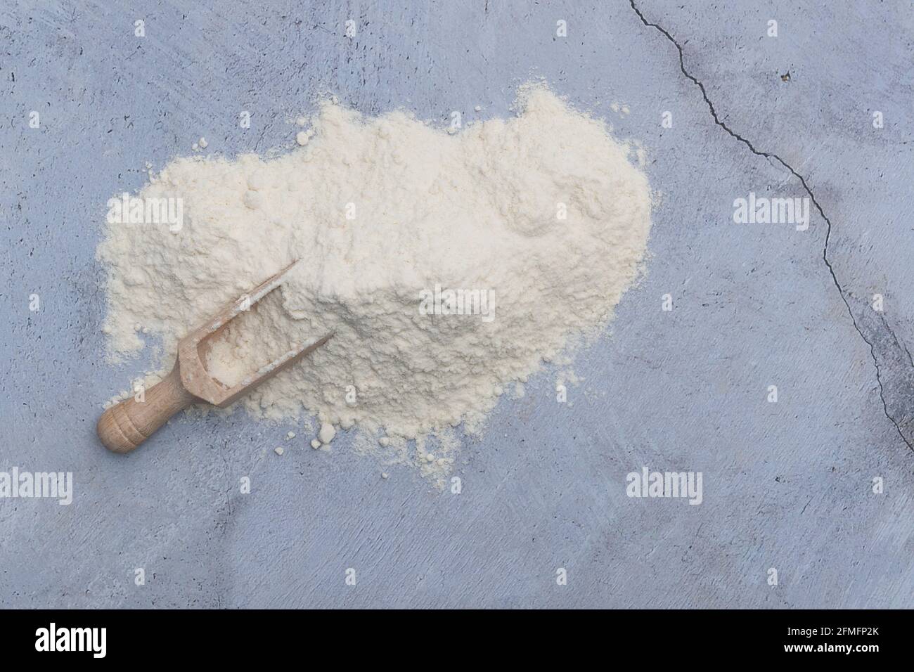 Farina bianca in polvere con cucchiaio di legno su tavola rustica in pietra. Foto Stock