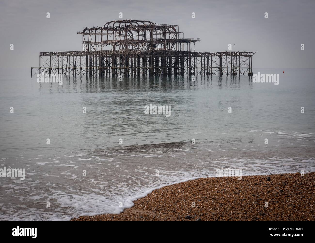 Le tristi rovine del West Pier di Brighton su un insolitamente mare calmo Foto Stock