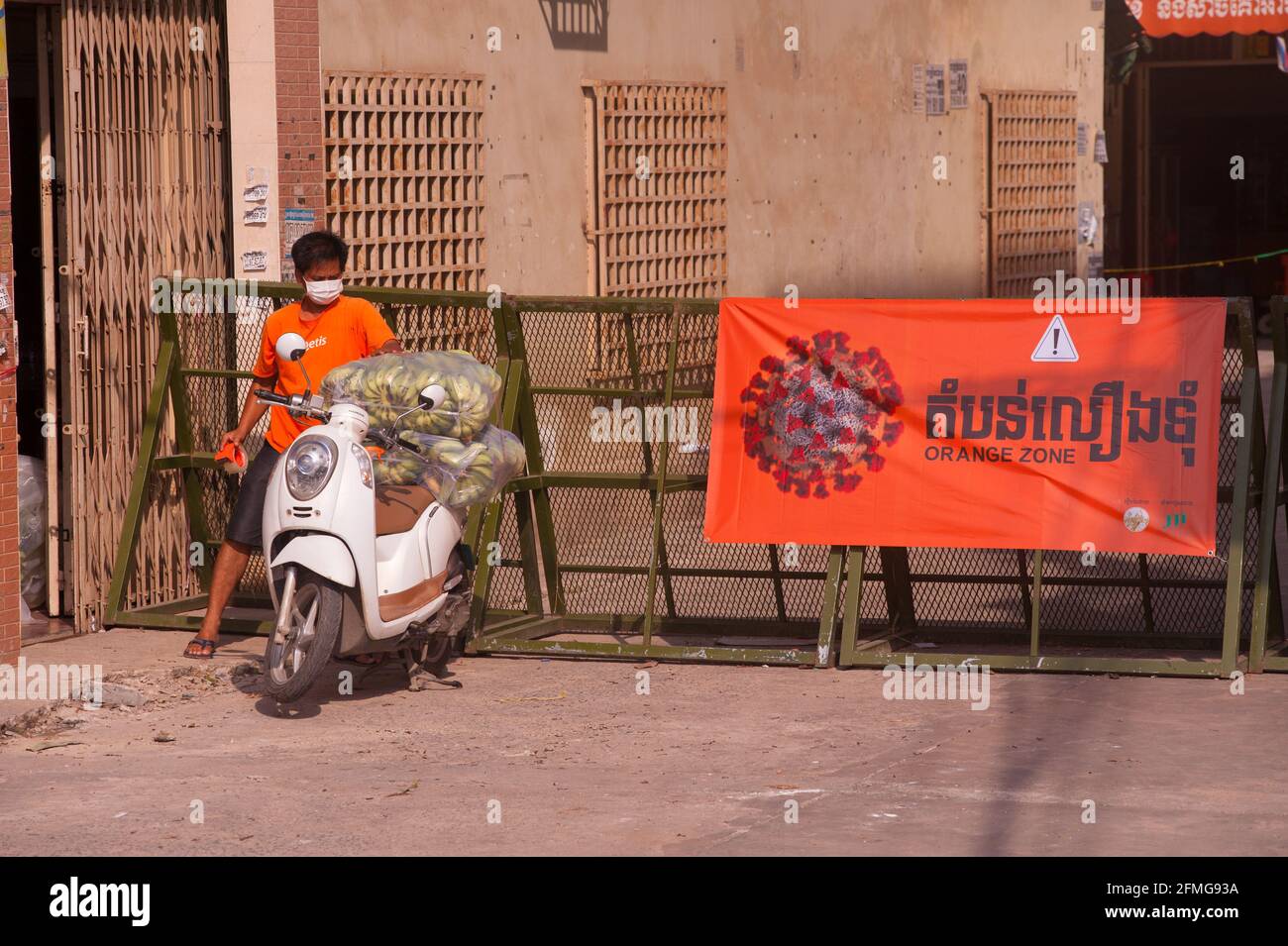 Phnom Penh, Cambogia. 9 maggio 2021. Un uomo cambogiano sta facendo del suo meglio per far sapere alla gente che sta consegnando banane da una zona arancione, indossando una T-shirt arancione e utilizzando nastro arancione. Dopo 3 settimane di chiusura totale della città, il governo ha diviso Phnom Penh in 3 zone colorate (Rosso, arancione e giallo) a causa del continuo aumento di COVID. Un checkpoint della polizia all'ingresso di una 'zona arancione', che significa medio rischio di infezione. Credit: Kraig Lieb / Alamy Live News Foto Stock