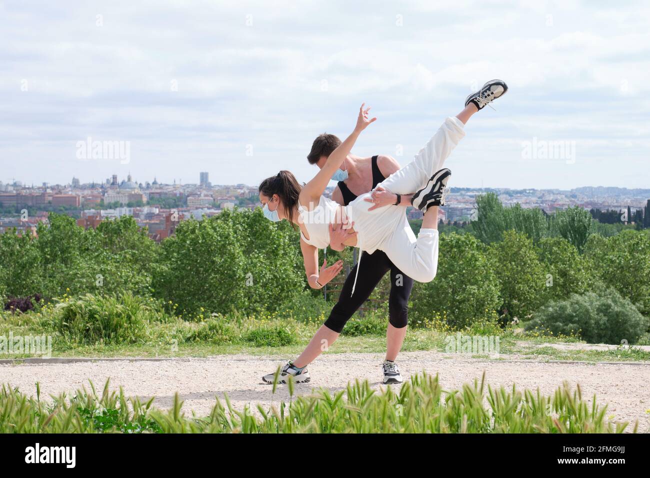 Giovane coppia che pratica la danza di strada, balletto, passi da ballo, movimenti in un parco che indossa maschere di protezione del viso. Foto Stock