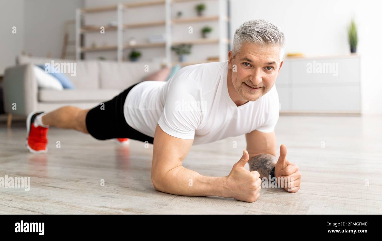 Allenamento domestico. Uomo maturo sportivo in piedi in tavola a gomito e rinforzando i muscoli abs, facendo allenamento fitness Foto Stock