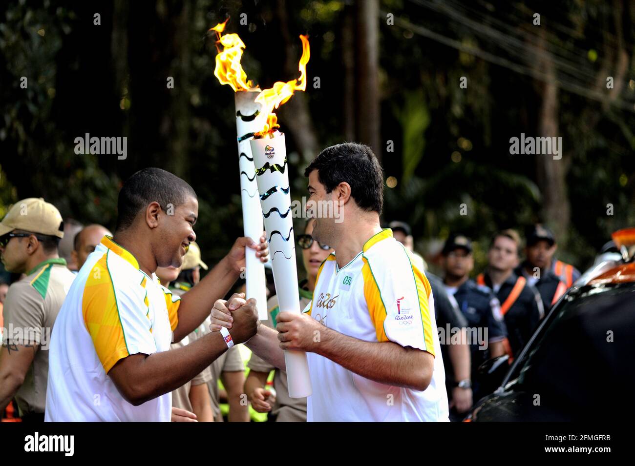 Olimpiadi, Rio de Janeiro, Brasile – 5 agosto 2016: Il portacolori della torcia trasferisce la fiamma al successivo in un ultimo giorno di relè della torcia olimpica di Rio 2016 Foto Stock