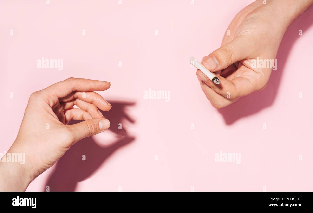 Passare la sigaretta di cannabis di mano in mano. Concetto di fumo di cannabis. Foto color pastello delle mani che si danno a vicenda sigaretta di carta sbriciolante Foto Stock