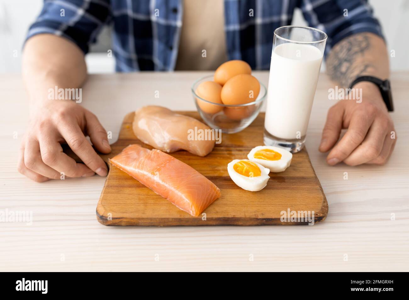 Mangiare sano. Uomo che prepara la colazione, seduto a tavola con filetto di carne crudo, pesce, latte e uova su tavola di legno Foto Stock