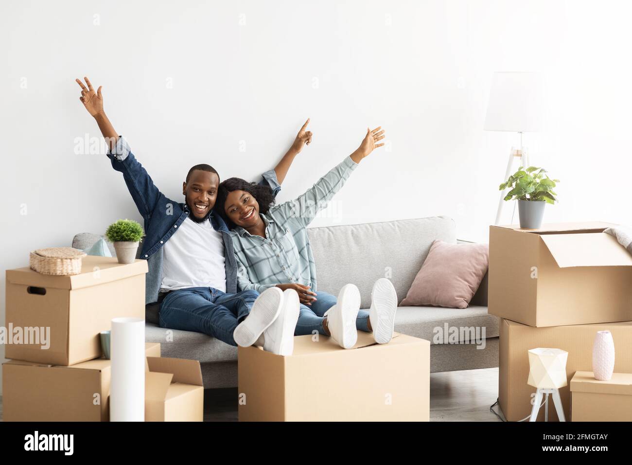 Felici proprietari. Gioioso sposi neri che si rilassano sul divano tra le scatole dopo il rilocamento Foto Stock