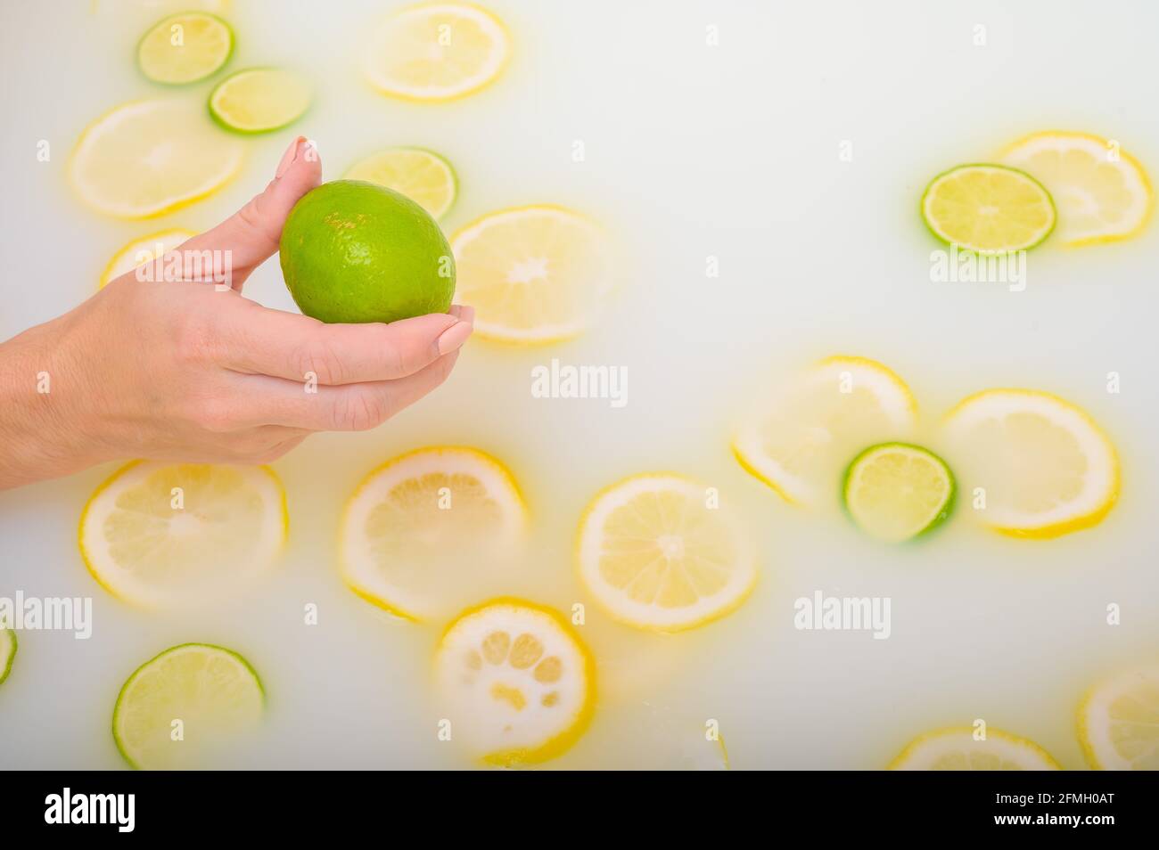 Primo piano di una mano femminile che tiene un calce su bianco acqua con fette di limone Foto Stock