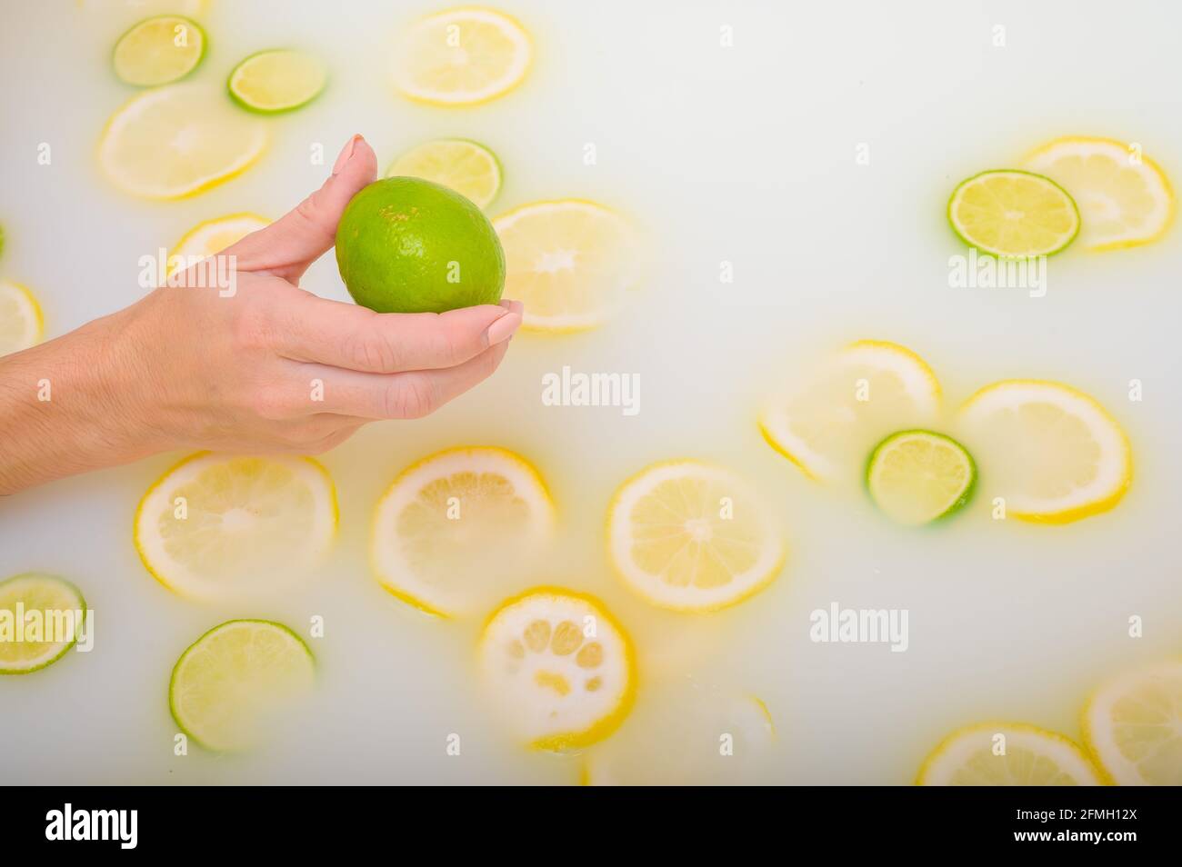 Primo piano di una mano femminile che tiene un calce su bianco acqua con fette di limone Foto Stock