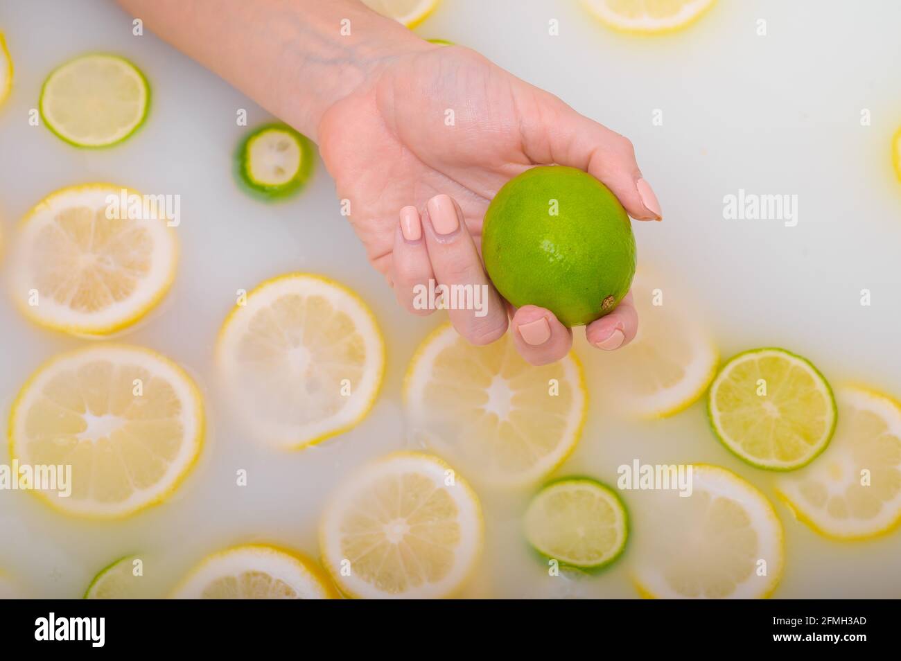 Primo piano di una mano femminile che tiene un calce su bianco acqua con fette di limone Foto Stock