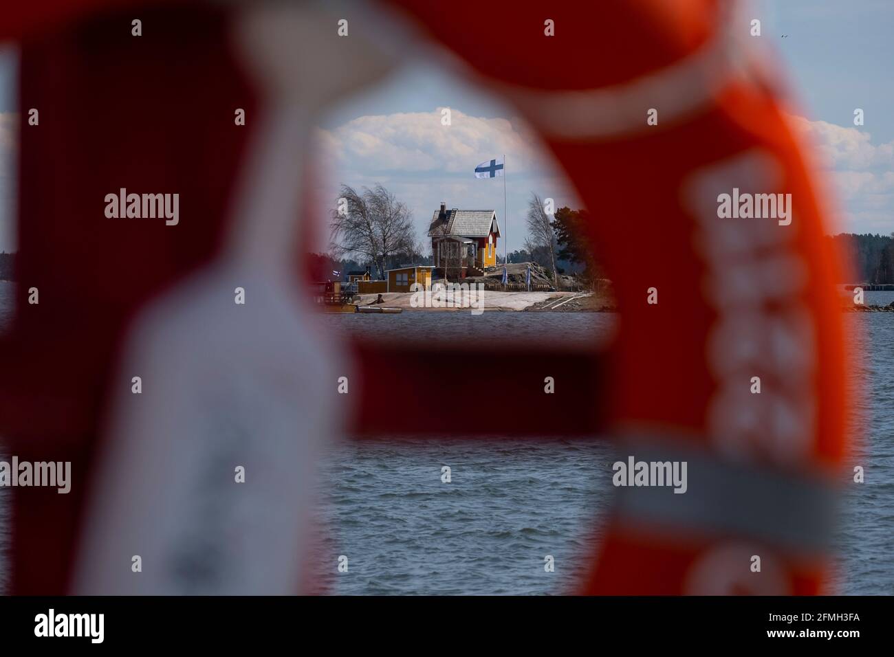 Helsinki / Finlandia - 9 MAGGIO 2021: Una piccola casa di legno con bandiera finlandese che rinuncia ad un flagpole. Scatta attraverso un anello salvavita. Foto Stock