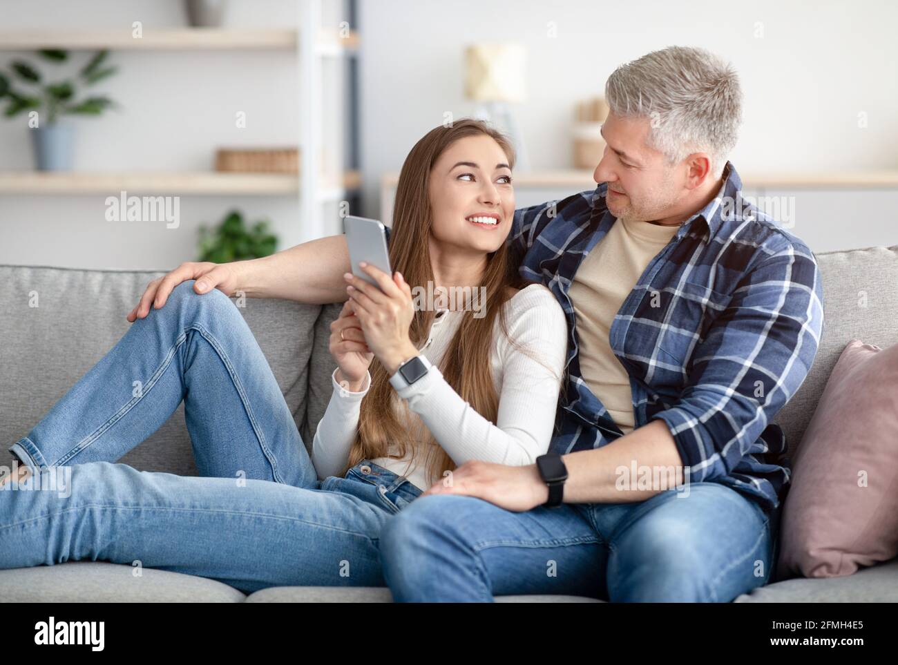 Coppia matura allegra che usa il moderno telefono cellulare a casa Foto Stock