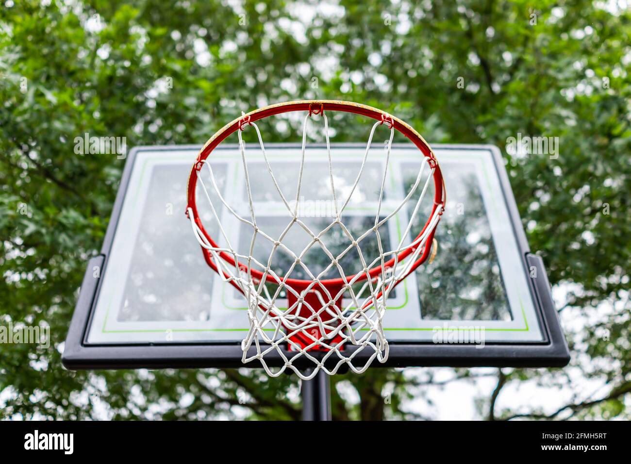 Primo piano guardando in su sotto il cerchio rosso di basket con la rete e. tavola di vetro nel parco giochi che si affaccia sul cielo e la casa in background Foto Stock