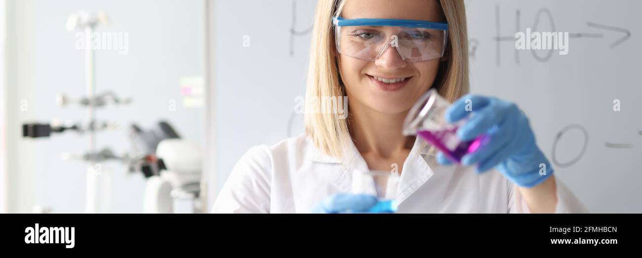 Donna chimico in occhiali protettivi versando liquido dalla beuta Foto Stock