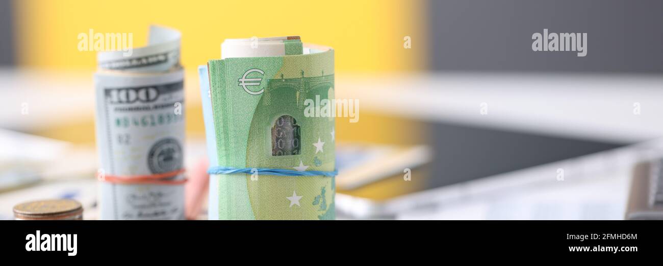 Carta arrotolata in dollari e in euro e monete giacciono sul tavolo primo piano Foto Stock