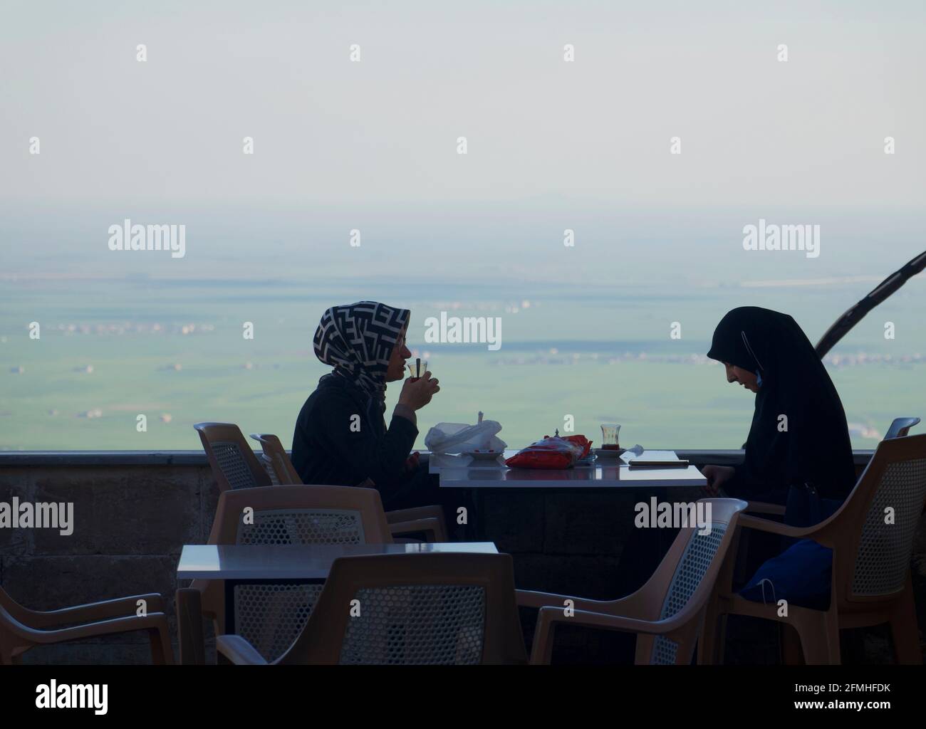 Due Signore in hijab bere tè con vista sulla pianura mesopotamiana e Siria, Mardin, Turchia Foto Stock