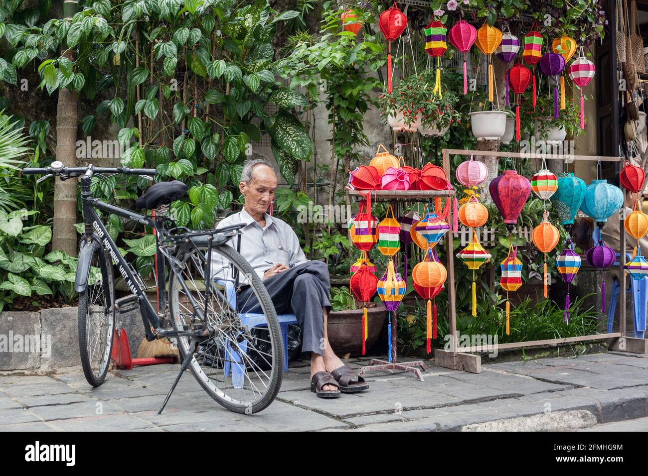 Il Signore vietnamita siede sul marciapiede che vende le lanterne colorate nella città vecchia, Hoi An, Vietnam Foto Stock