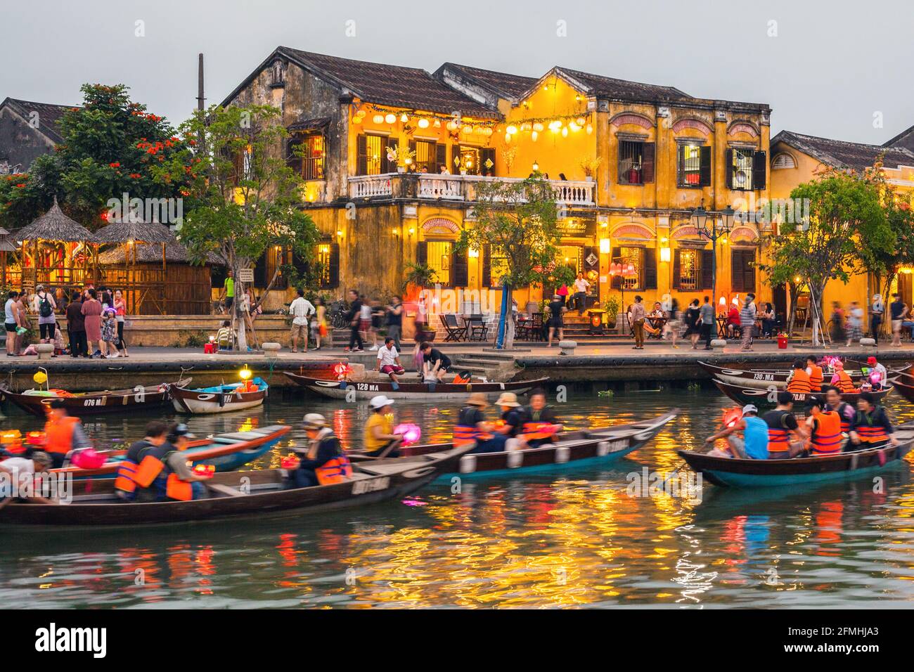 Luci colorate riflesse sull'acqua mentre le barche viaggiano lungo il fiume nella città vecchia, Hoi An, Vietnam Foto Stock