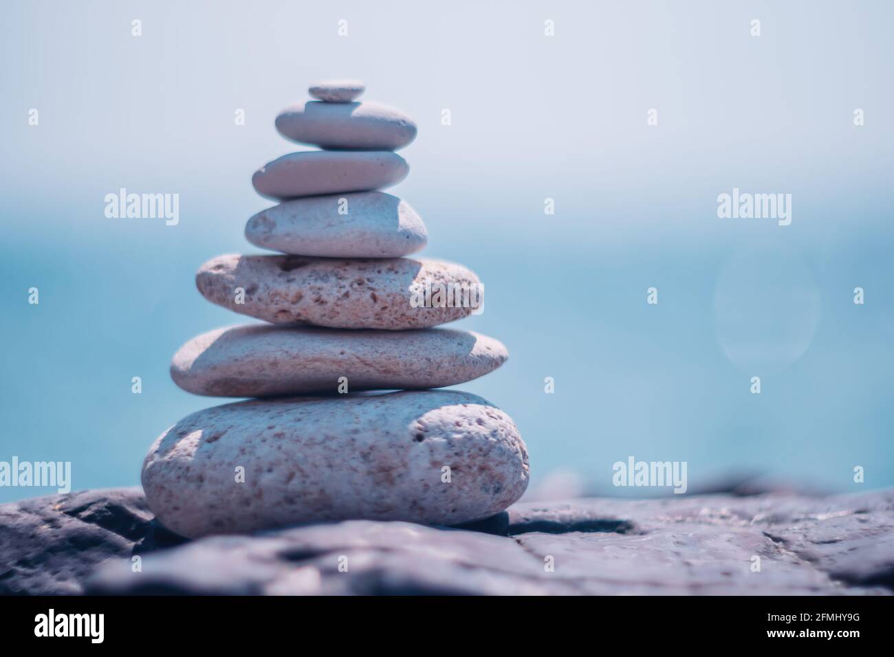 Equilibrata piramide di ciottoli sulla spiaggia in una giornata di sole. Abstract Sea bokeh sullo sfondo. Messa a fuoco selettiva. Pietre Zen sulla spiaggia di mare, meditazione Foto Stock