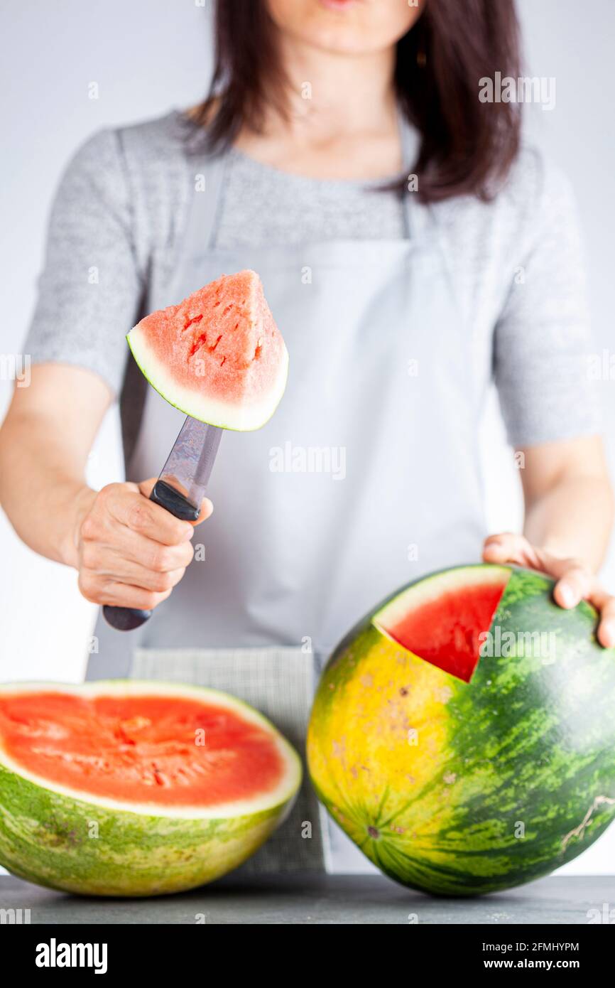 Una giovane donna caucasica sta tagliando un cuneo da un cocomero maturo usando un coltello. Il melone è maturo con la macchia di campo. Frutta di stagione estiva leggera e ariosa c Foto Stock