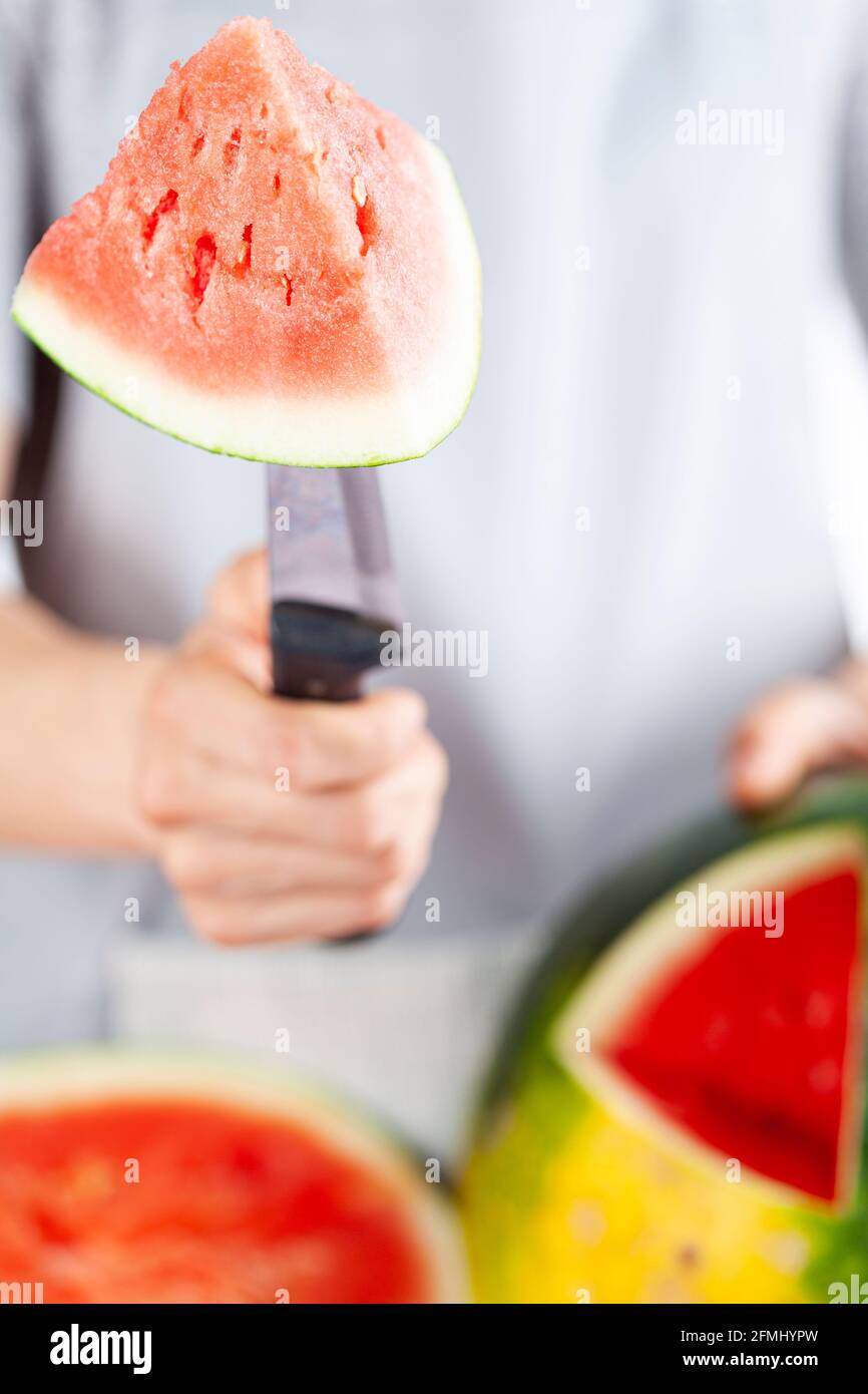 Una giovane donna caucasica sta tagliando un cuneo da un cocomero maturo usando un coltello. Il melone è maturo con la macchia di campo. Frutta di stagione estiva leggera e ariosa c Foto Stock
