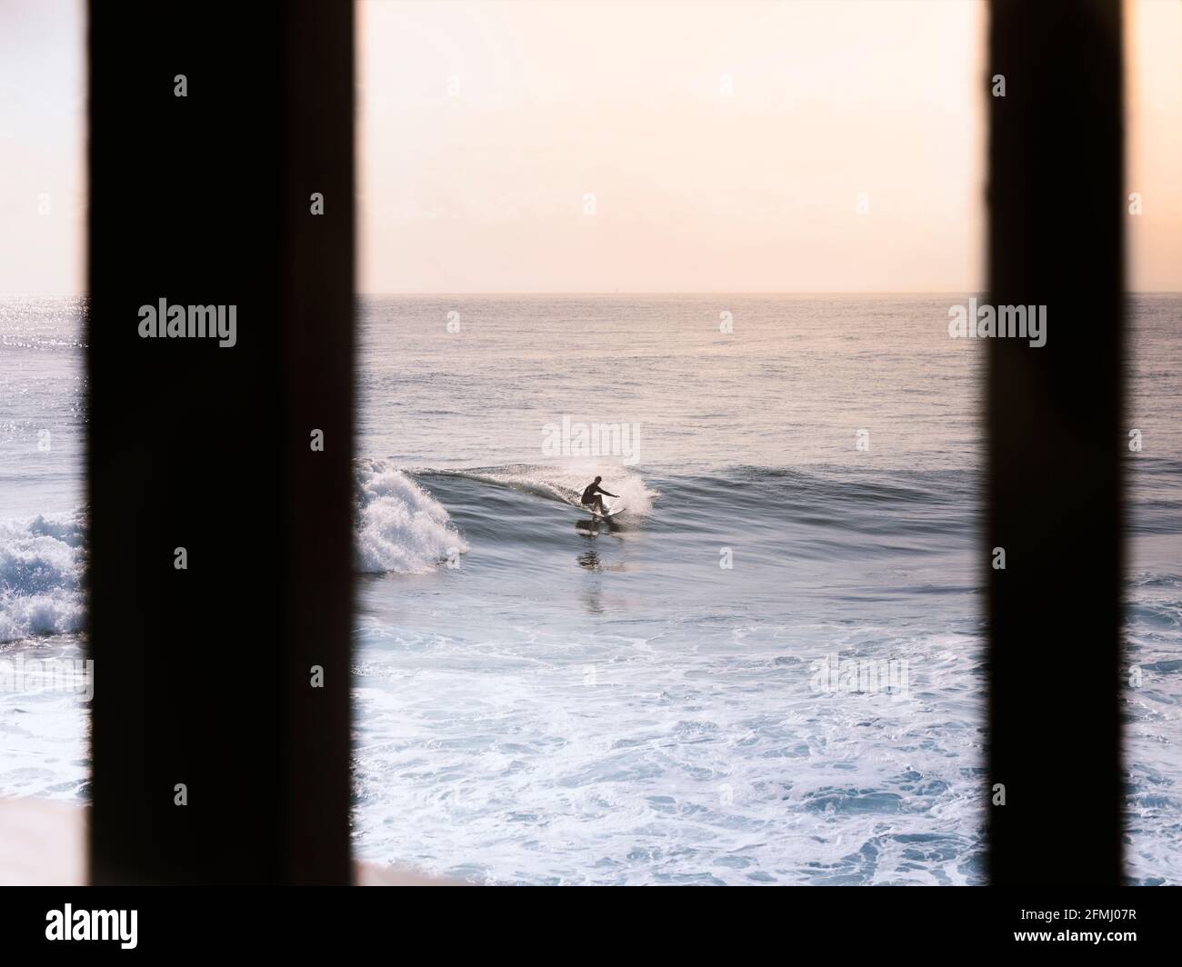 Surfista irriconoscibile che cavalca onde di mare azzurro sotto il rosa chiaro cielo in prima serata Foto Stock