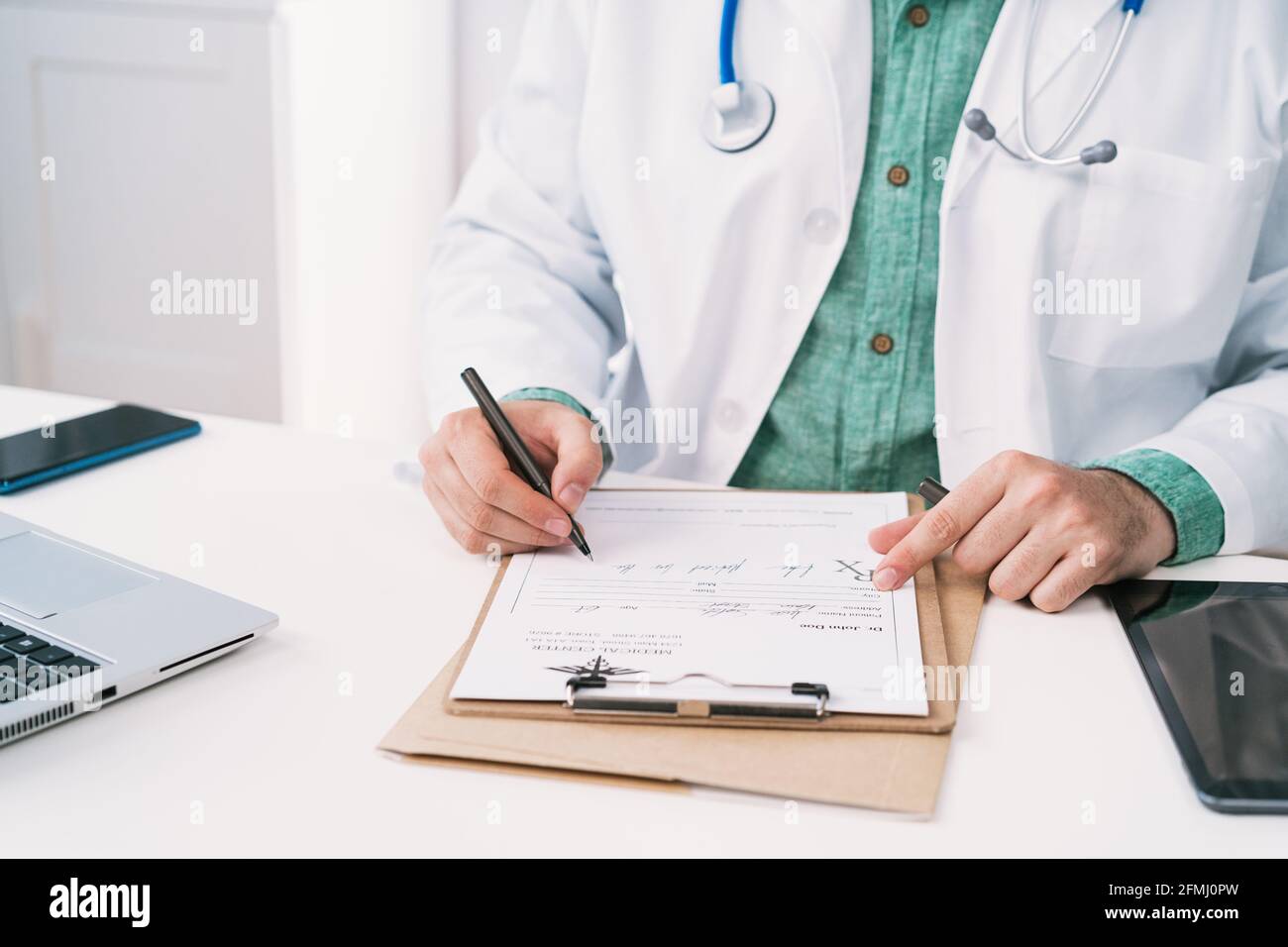 Uniforme non riconoscibile ritagliata con stetoscopio che prende appunti su un foglio di carta durante il lavoro in clinica Foto Stock