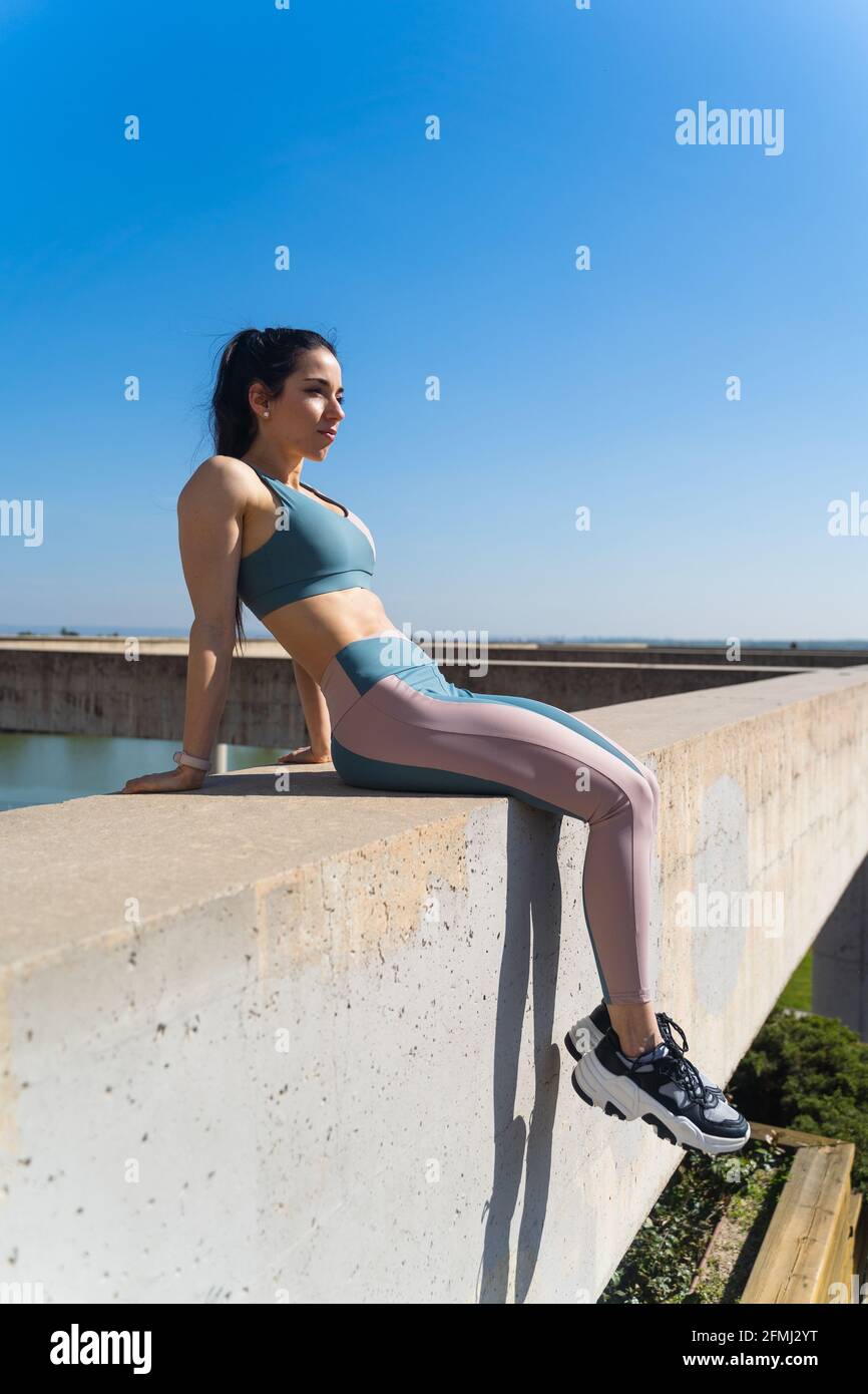 Vista laterale dell'atleta in vestiario sportivo lontano da recinto di cemento sotto il cielo blu Foto Stock