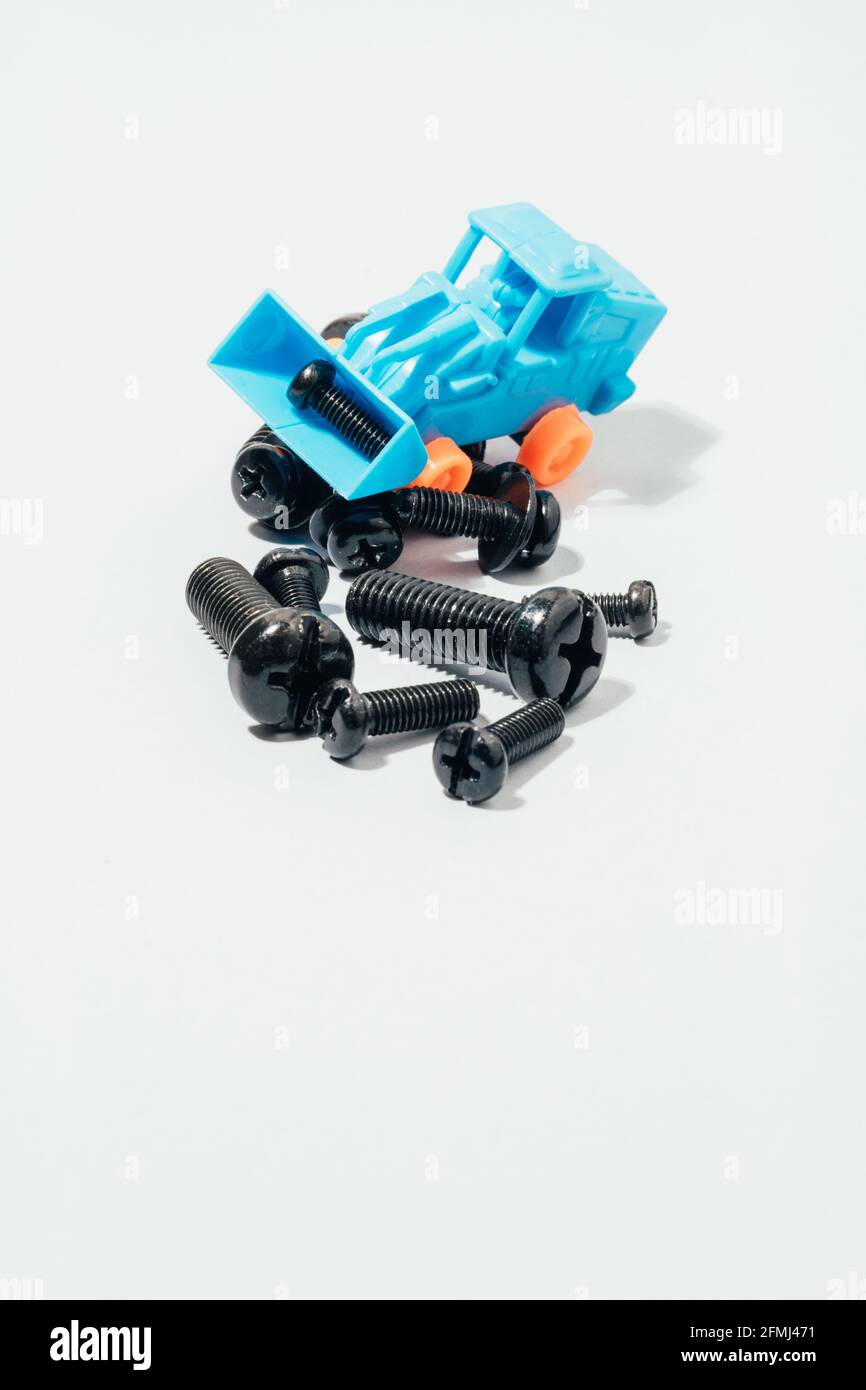 Dall'alto di un piccolo trattore giocattolo in plastica che raccoglie vari neri viti su tavola bianca Foto Stock