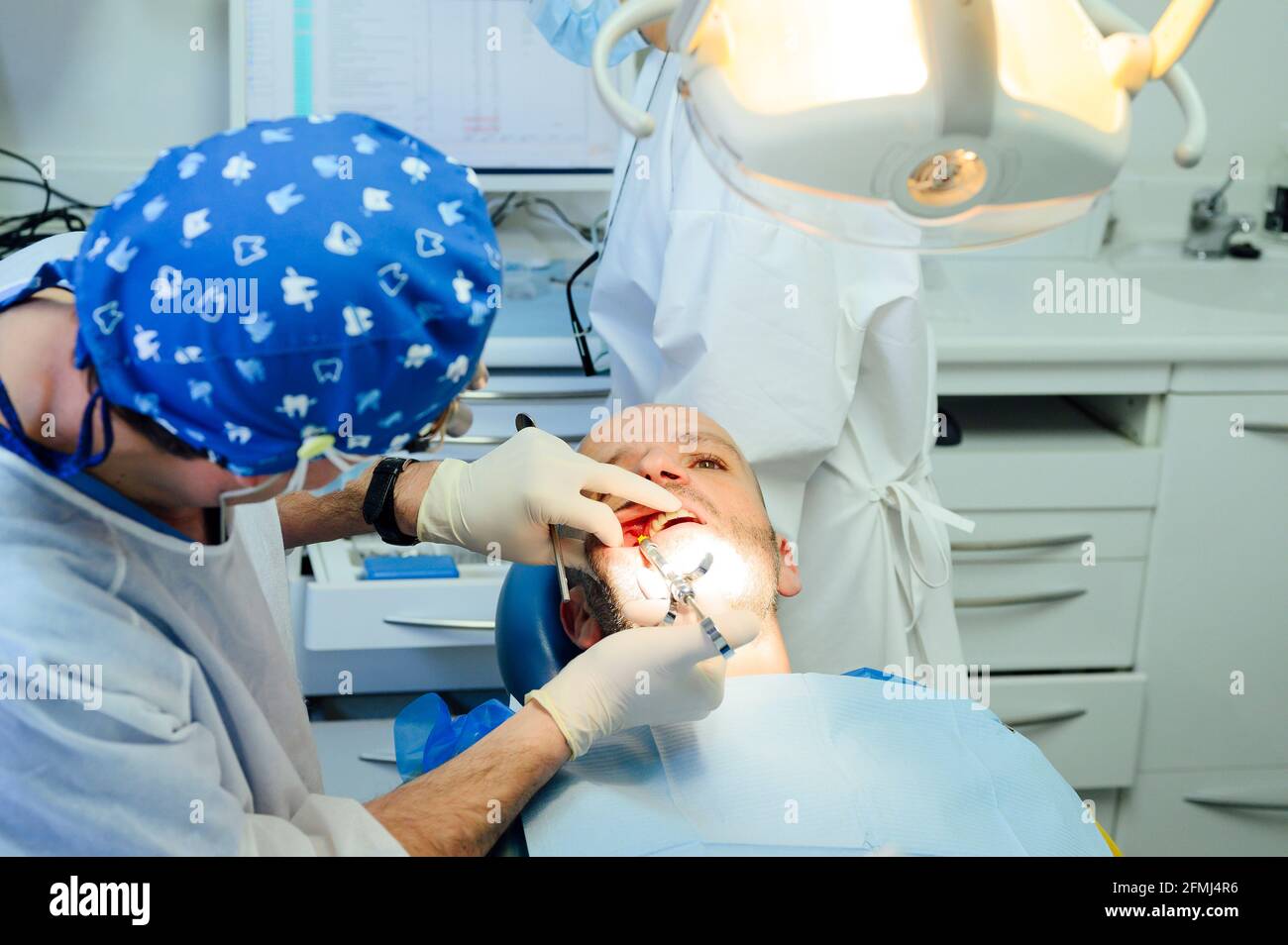 Vista laterale del chirurgo dentale anonimo in uniforme e medico binocoli con contenuto uomo sulla sedia in clinica Foto Stock