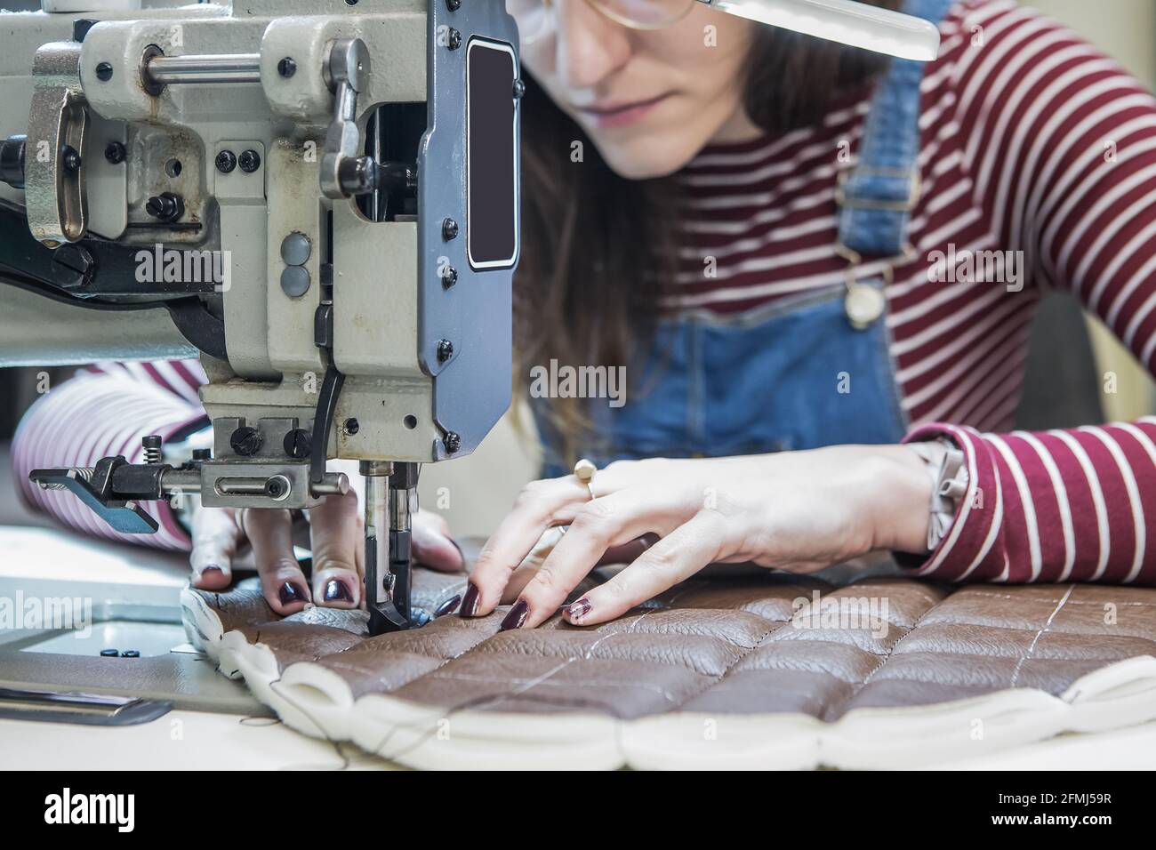 Artigiana femminile che usa la macchina da cucire mentre crea la tappezzeria per moto sedile in officina Foto Stock