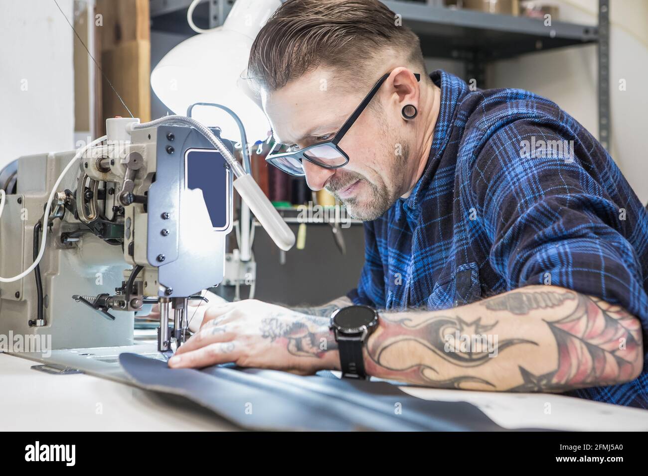 Uomo artigianale che usa la macchina da cucire mentre crea la tappezzeria per moto sedile in officina Foto Stock