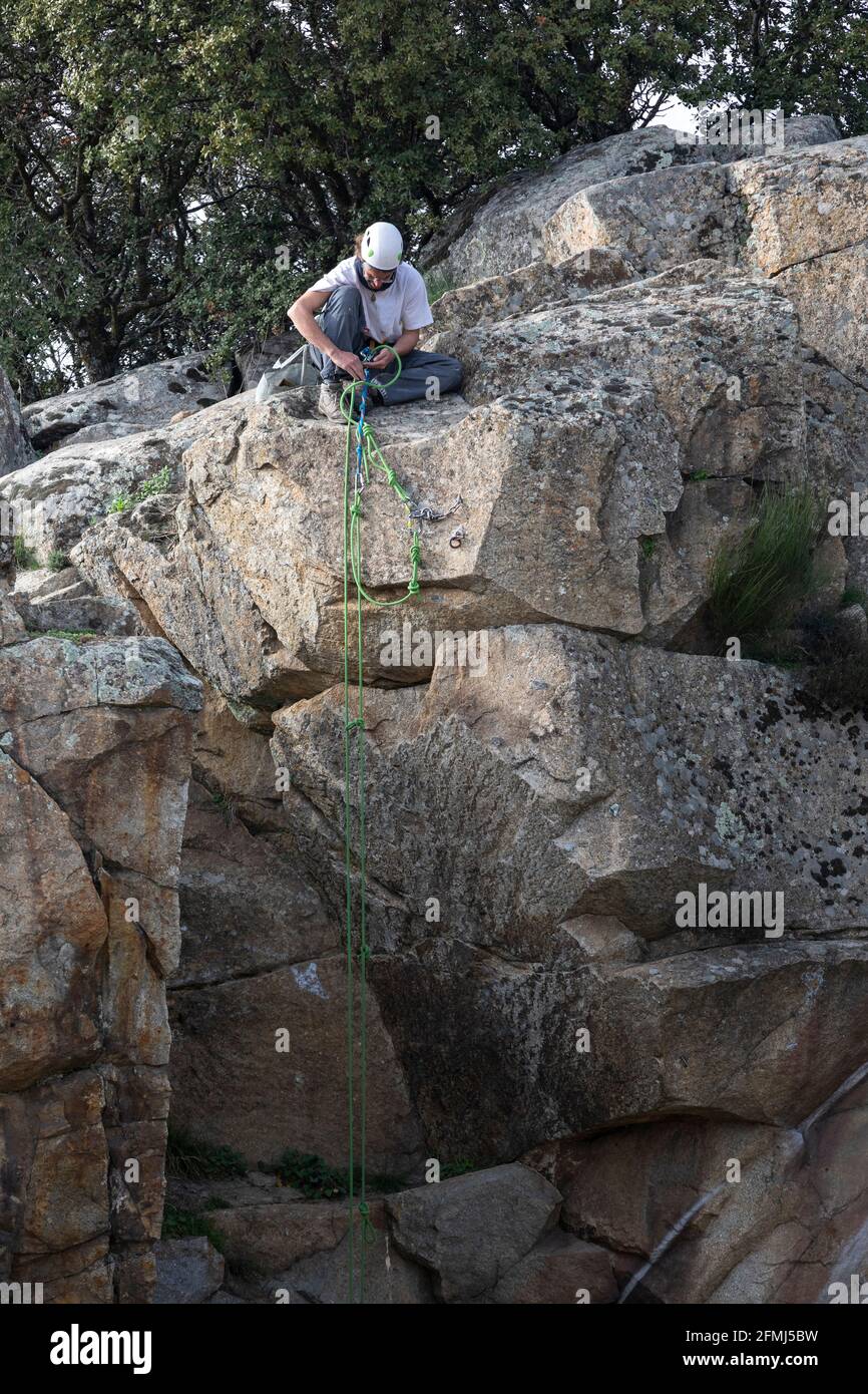 Arrampicatore maschio in casco protettivo seduto su roccia e fissaggio imbracatura prima della discesa dalla montagna Foto Stock
